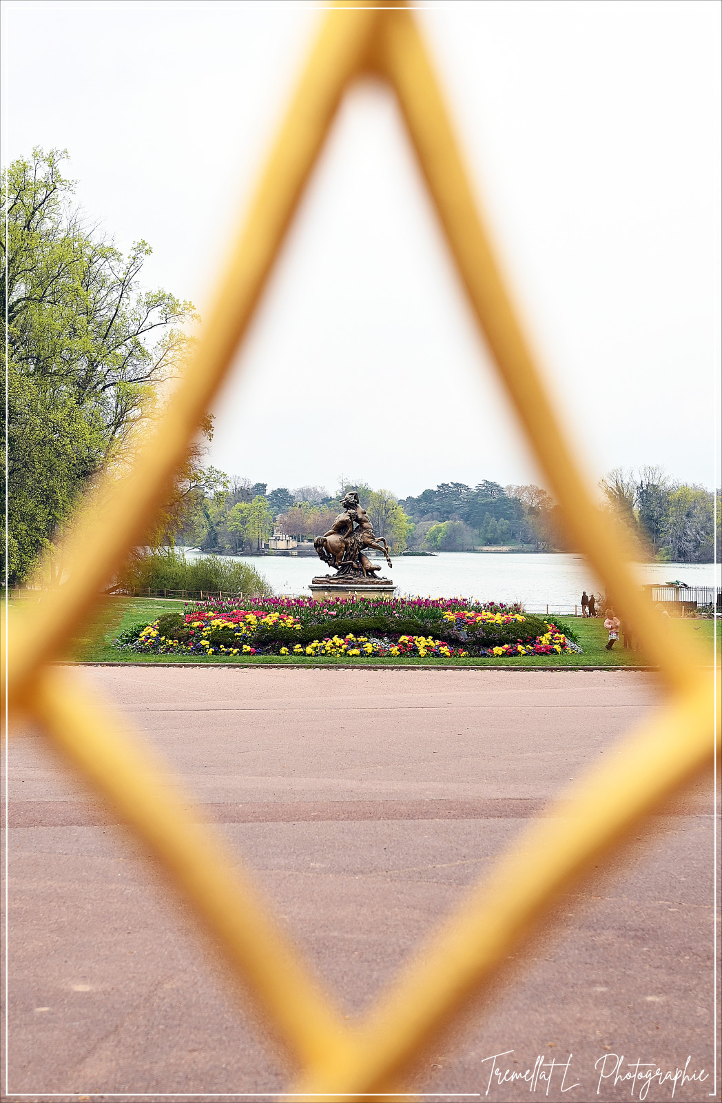 À travers les losanges dorés de la grille de la Porte des Enfants du Rhône, le regard se pose naturellement sur la statue de La Centauresse et le Faune.